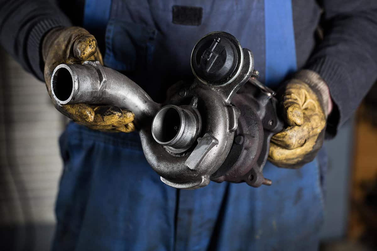 Car mechanic hands in garage with old and used turbocharger