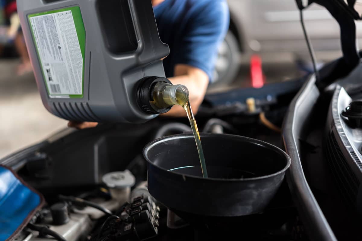 Car mechanic using a funnel to put new oil to the car engine