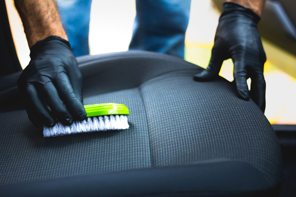 Car owner cleaning the car seat using a small green brush