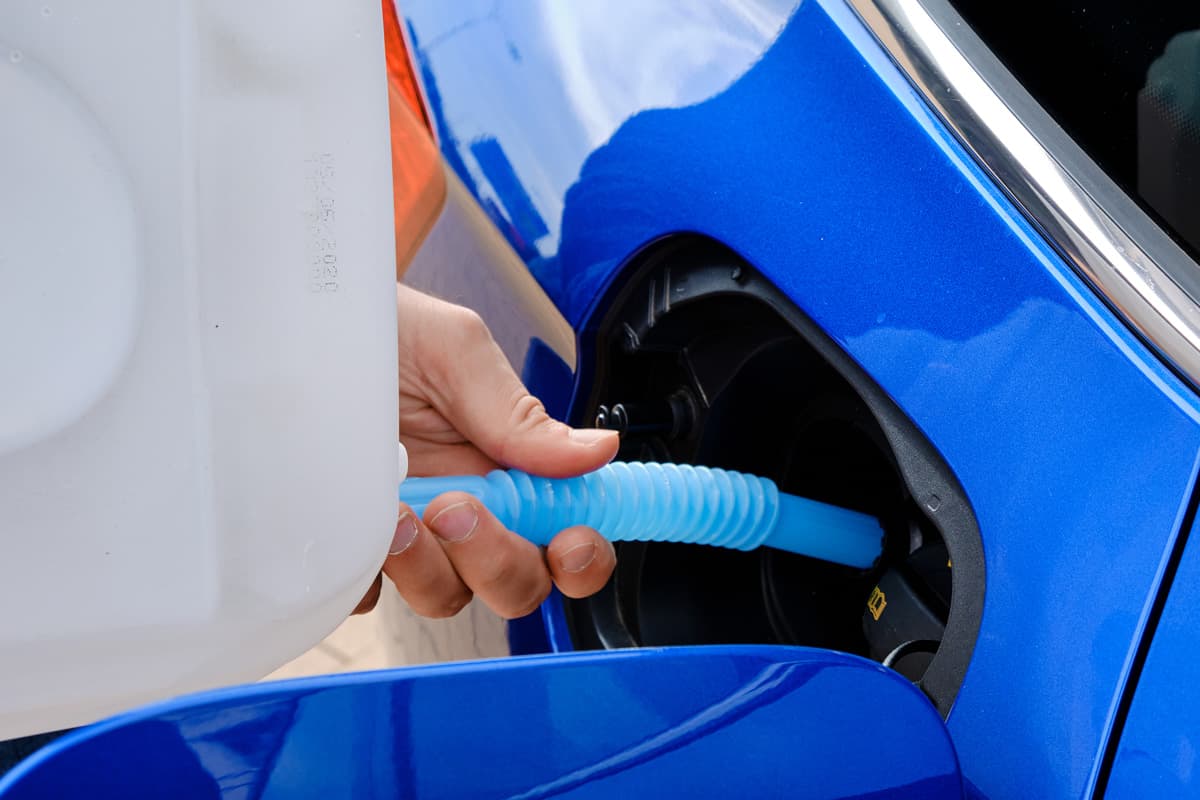 Close up filling of diesel exhaust fluid from canister into the tank of blue car for reduction of air pollution. Environmental or eco friendly solution. 