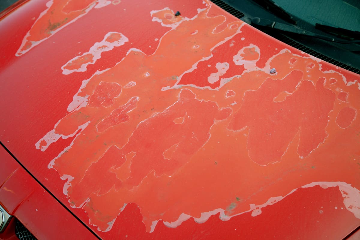 Damaged paintwork on the hood or bonnet of a red car.