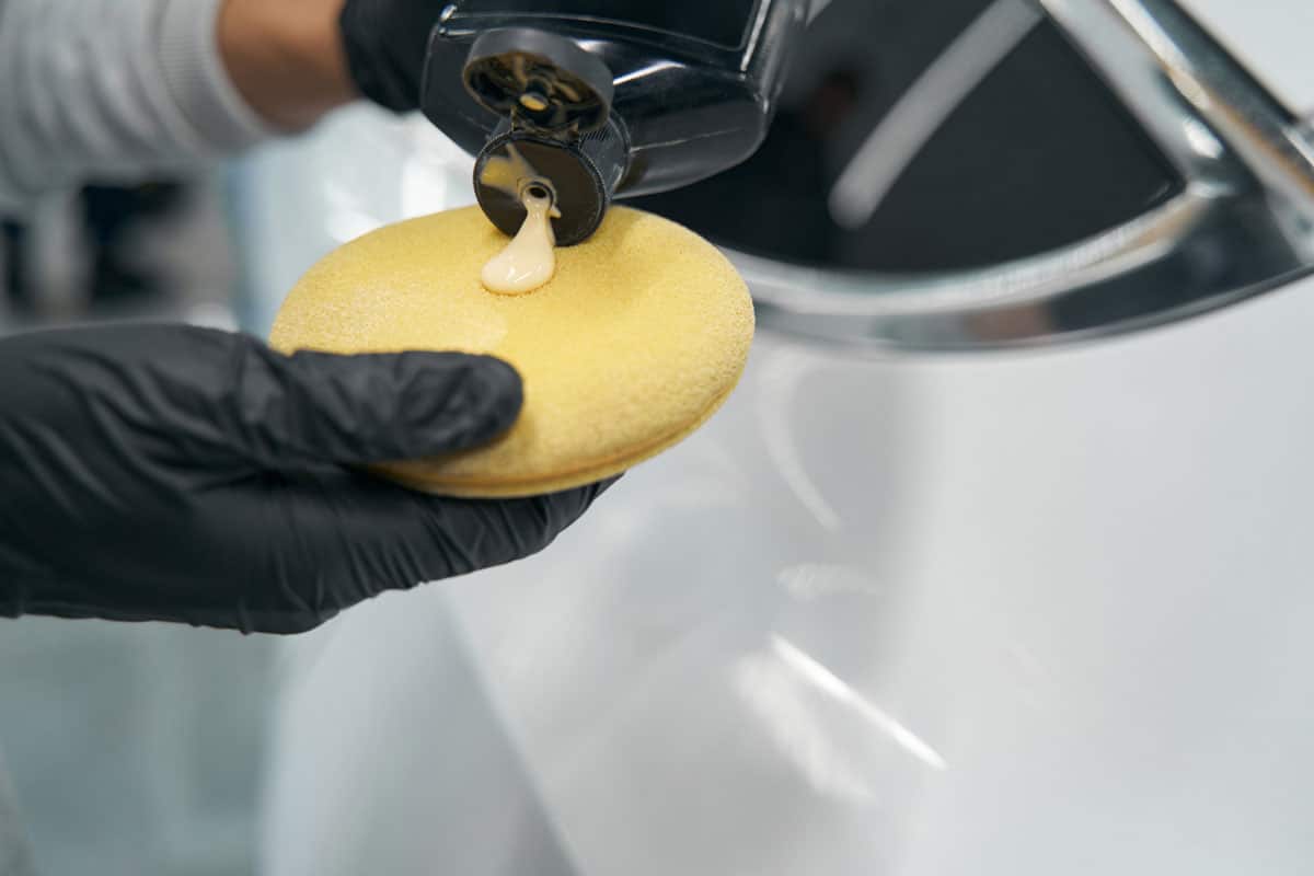 Gloved hands applying liquid wax on foam sponge