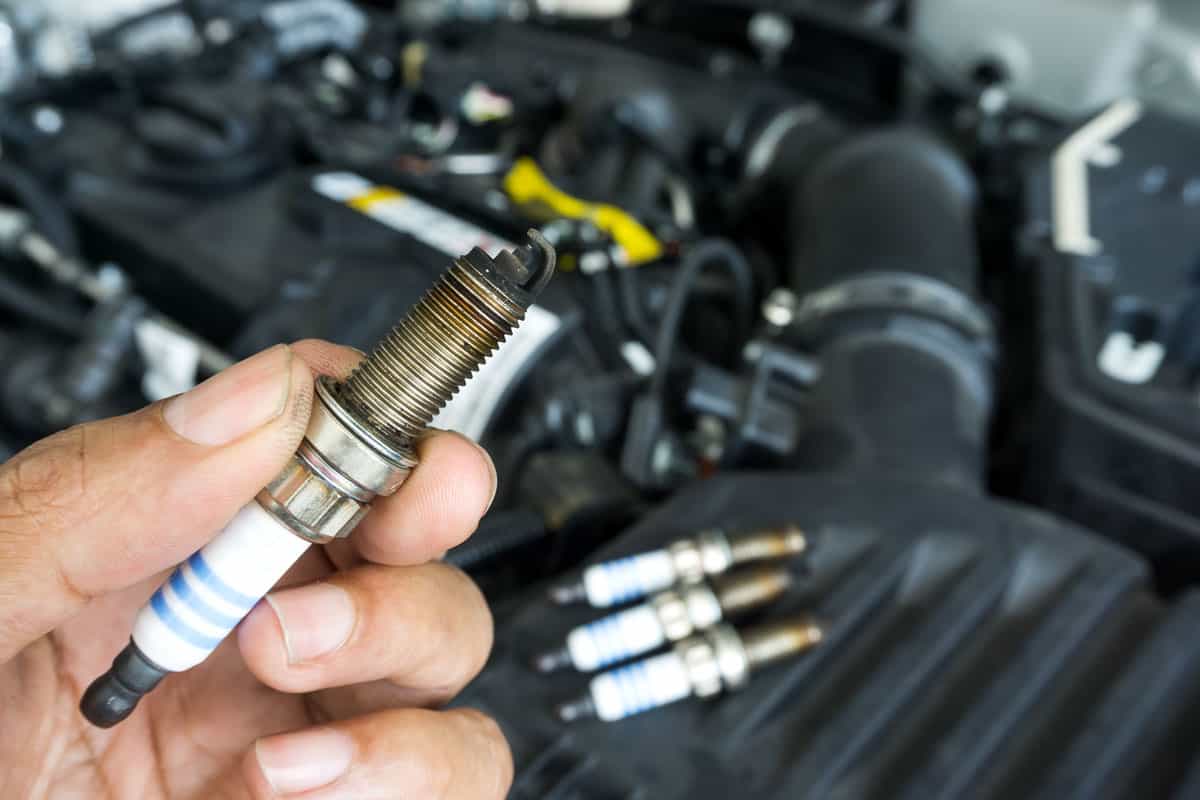 Hand of the auto mechanic holding the old spark plug on blurred engine car