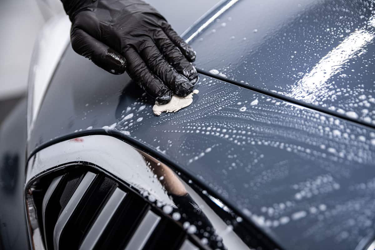Man car wash worker cleaning car varnish with car clay
