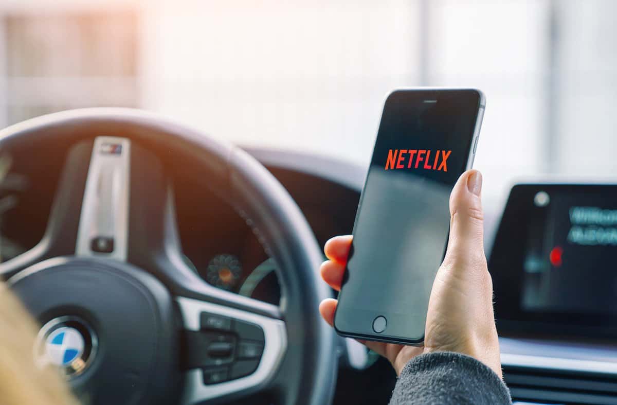 Man opening Netflix app on Apple iPhone in a car