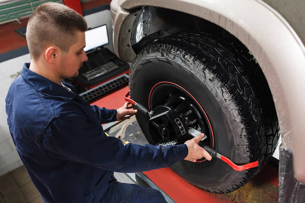 Mechanic tuning aligner for wheel alignment in garage closeup. Professional car maintenance in modern workshop