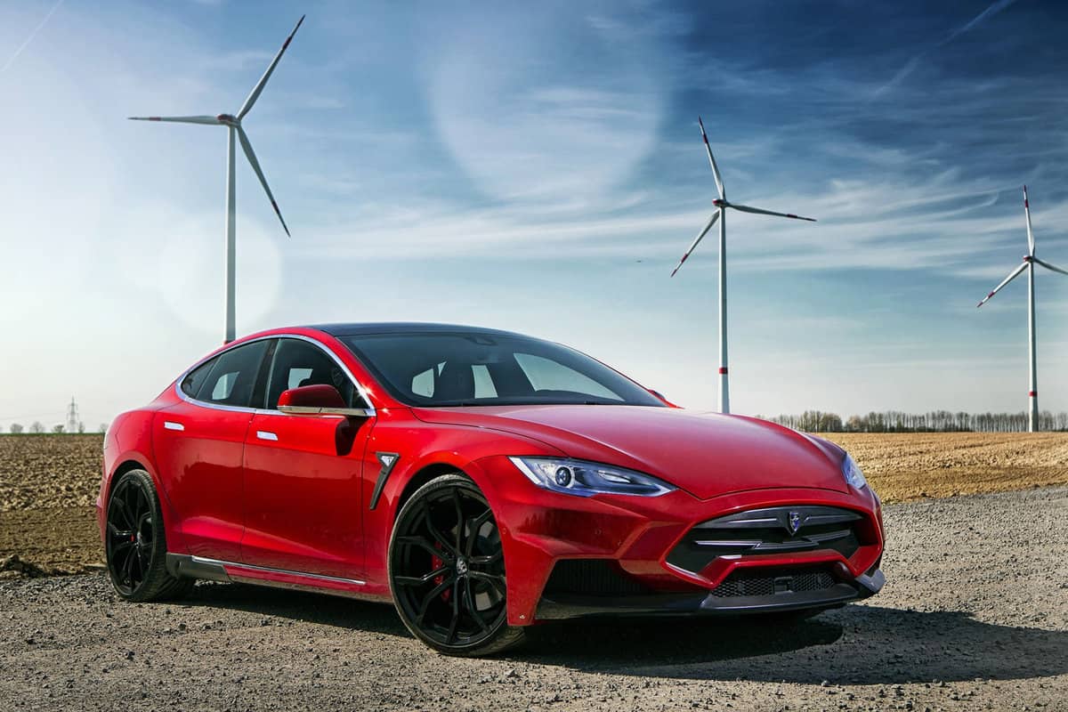 Photograph of a red Tesla model S in front of a windmill field.
