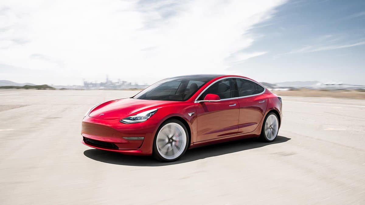 Red tesla model 3 in front of a distant city