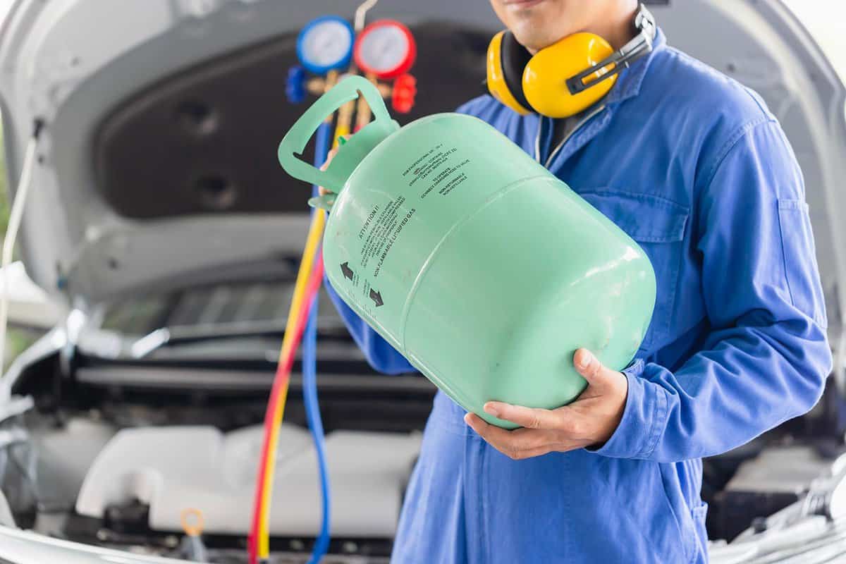 Technician with manifold tool gauge bucket refrigerant applies to car air conditioning