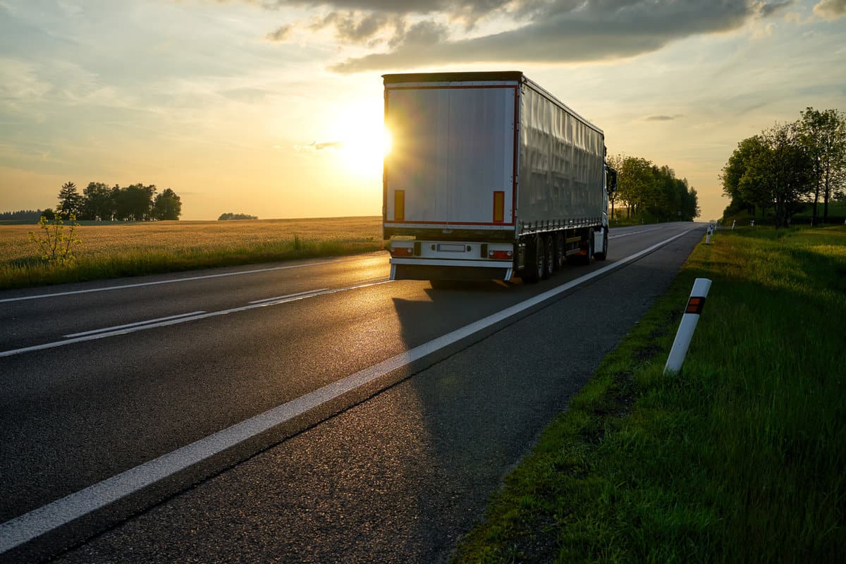 Truck departing towards the horizon on an asphalt road in a rural countryside at sunset.