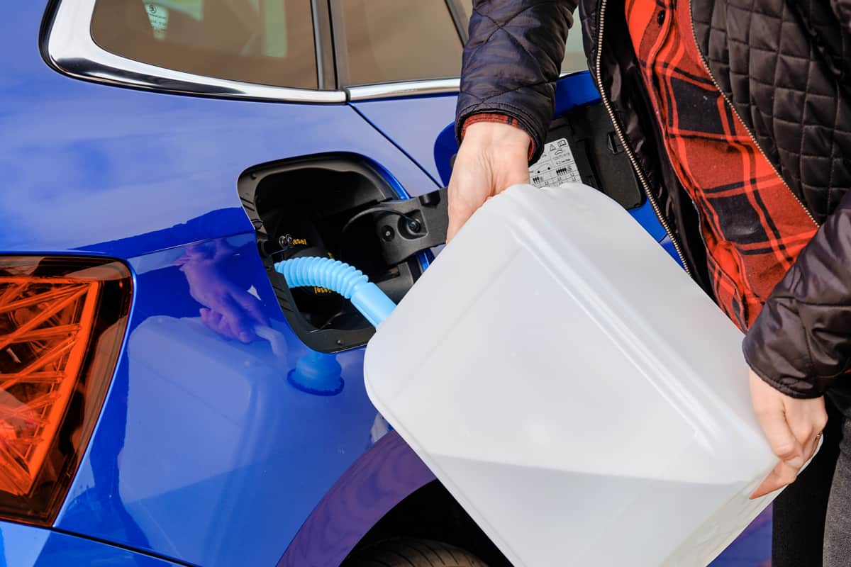 Woman filling a diesel engine fluid from canister into the tank of blue car. Diesel exhaust fluid for reduction of air pollution.