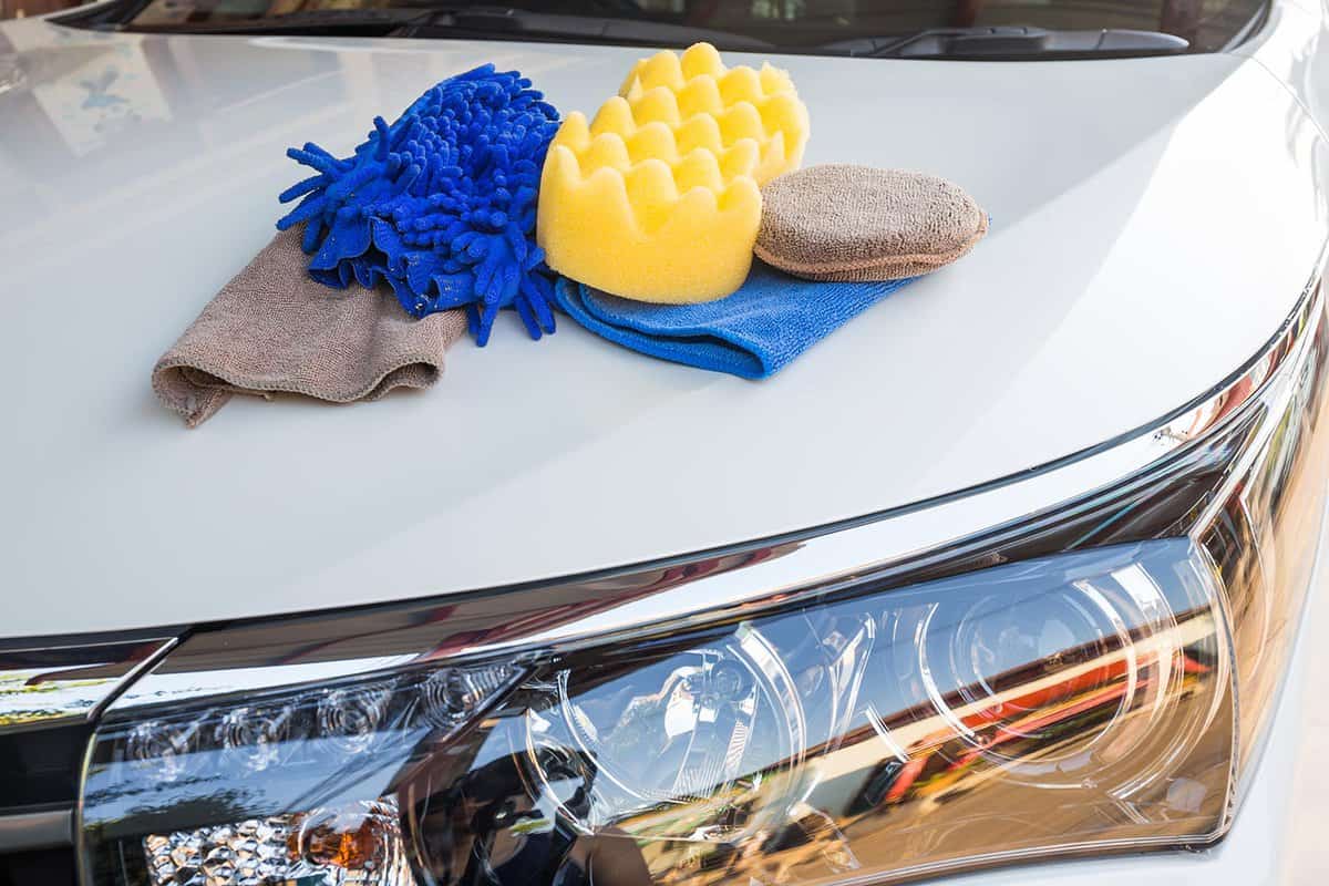 Yellow sponges and blue mitts for washing and microfiber fabric with cleaner cloth on white car