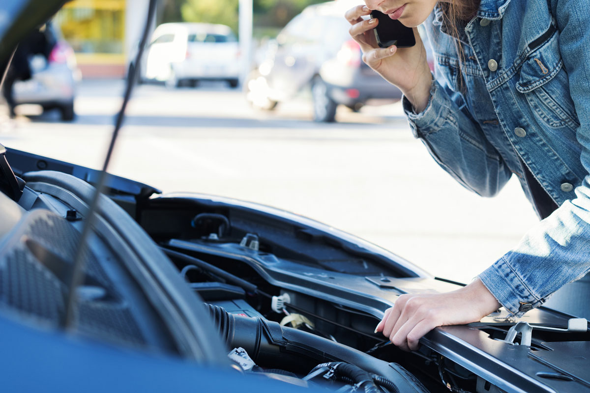 Young woman calling a car assistance service with her smartphone, her car has broken down
