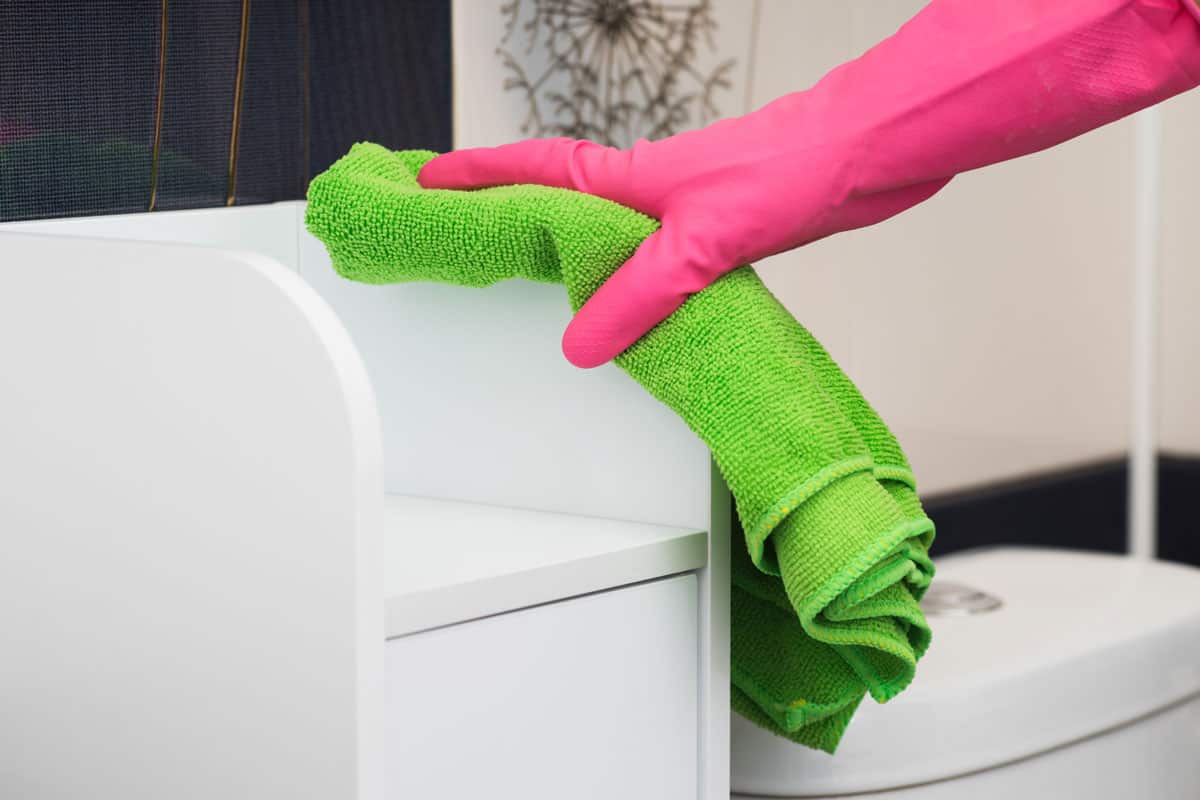 hand with pink gloves holding green duster microfiber cloth for cleaning