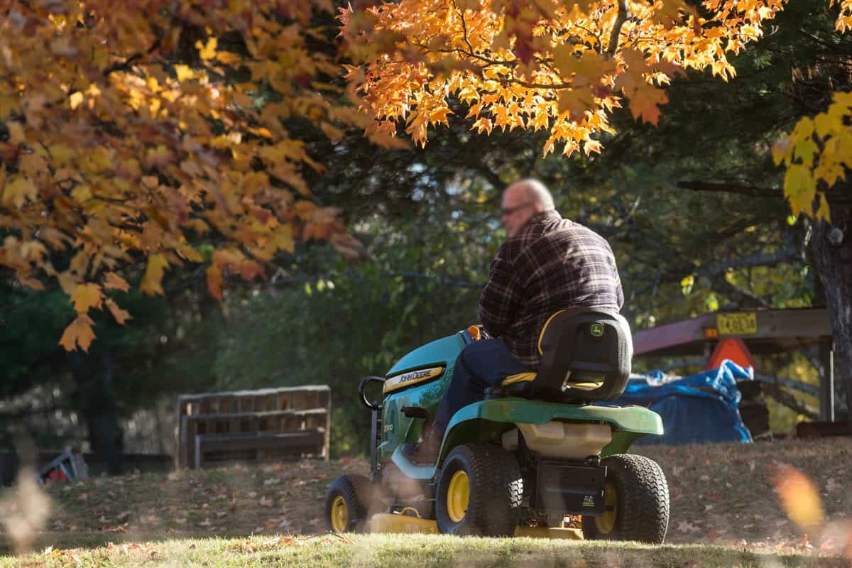A man mows his lawn with a John Deere lawn tractor on a warm Autumn afternoon