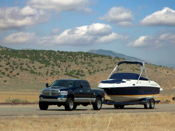 A truck tows a boat down a scenic road, Does My Truck Have A Tow Package [Here's How To Tell]