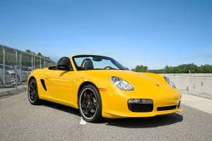 A yellow Porsche Boxster limited edition convertible with black wheels and red brake calipers parked on a blue sky day, What Is The Best Oil For Porsche Boxster?