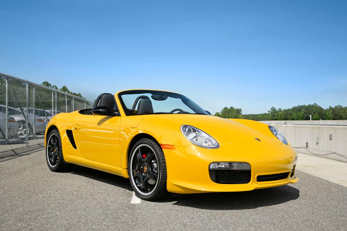 A yellow Porsche Boxster limited edition convertible with black wheels and red brake calipers parked on a blue sky day