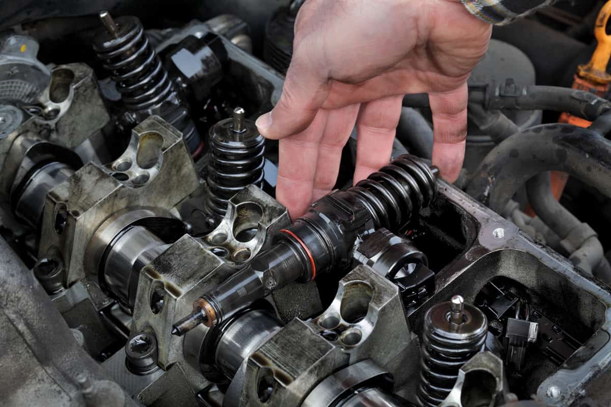 Car mechanic fixing modern diesel engine, closeup of hand removing injectors from cylinder head