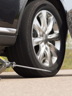 Jacking up a car to change a tyre after a roadside puncture with the hydraulic jack inserted under the bodywork raising the vehicle and the spare wheel balanced on the side - Can I Jack My Car/Truck On The Axle