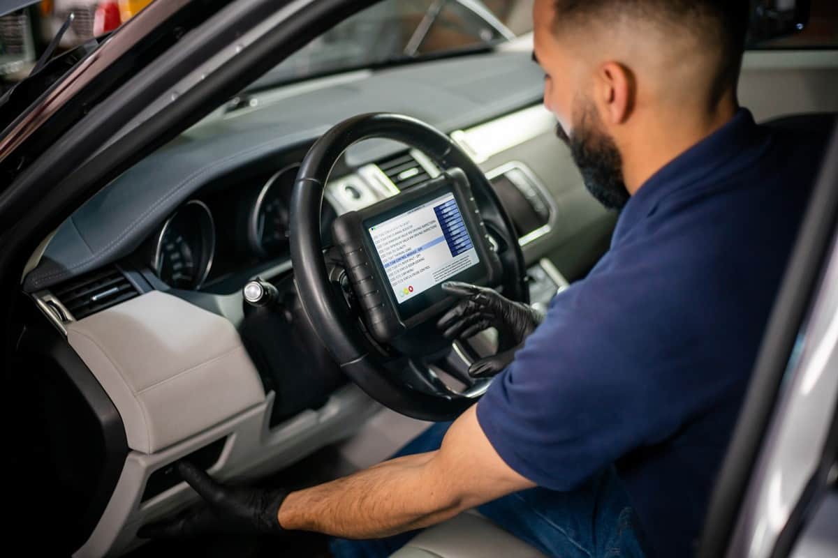 Male car engineer checking the car sensors using a tablet placed on the steering wheel of the car
