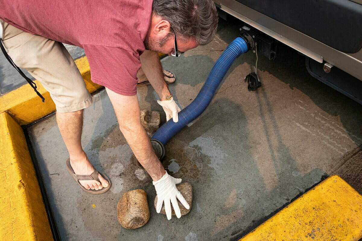 Man in latex gloves connects sewer hose to an RV dump station hole