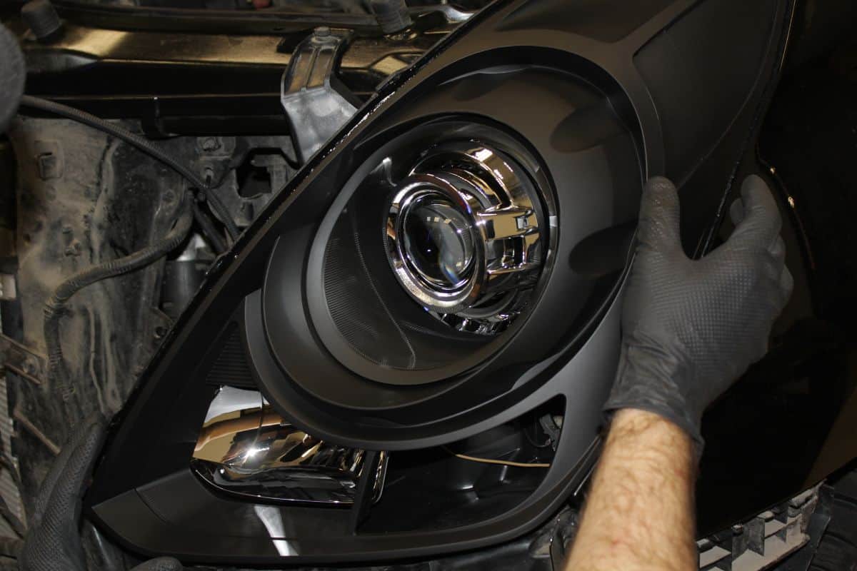 Mechanic, installs the headlight on the car. Repair of car headlights. Tuning and restoration of automotive optics. A mechanic wearing rubber gloves installs an LED lens into the headlight housing.