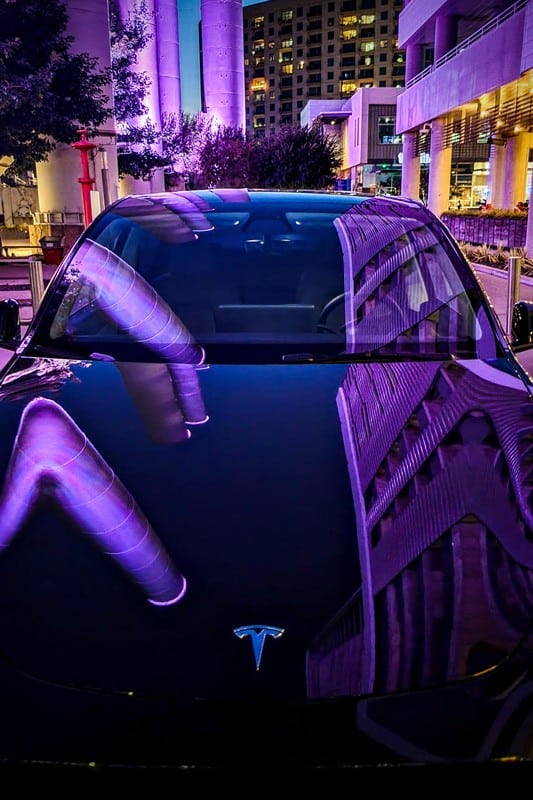 Tesla model 3 glowing in purple due to reflection of light from the buildings