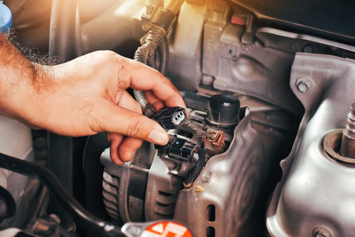 The auto mechanic hand is grasping the car alternator charger plug with sunlight