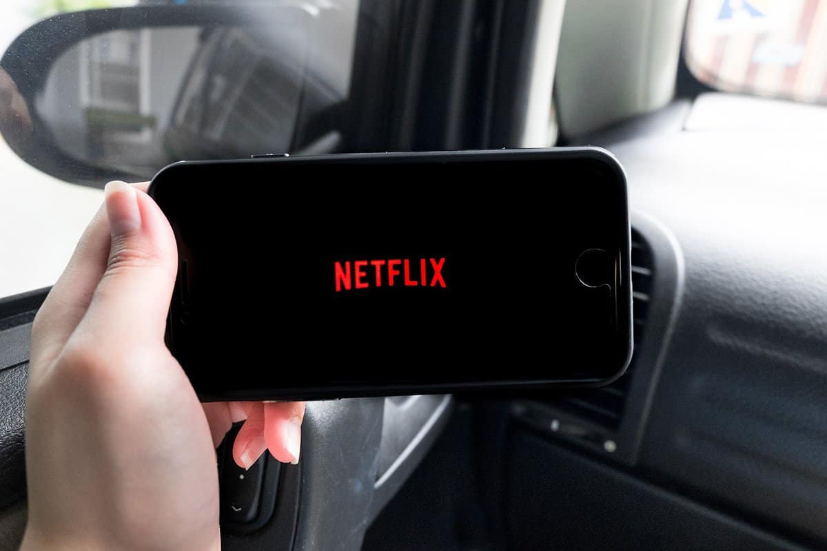 Woman hand holding iPhone screen showing Netflix logo in a car