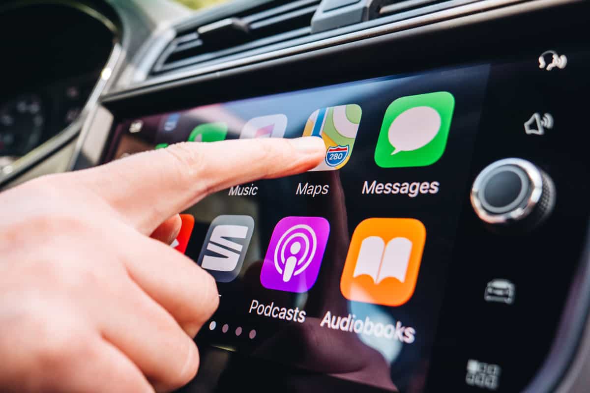 Woman pressing Apple Maps button on the Apple CarPlay main screen in modern car dashboard during driving on Spanish holiday highway