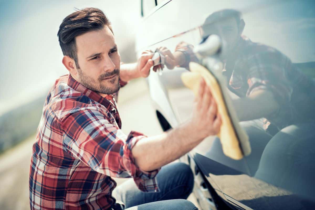 Young man cleaning his car outdoors.Man with a microfiber wipe the car polishing.