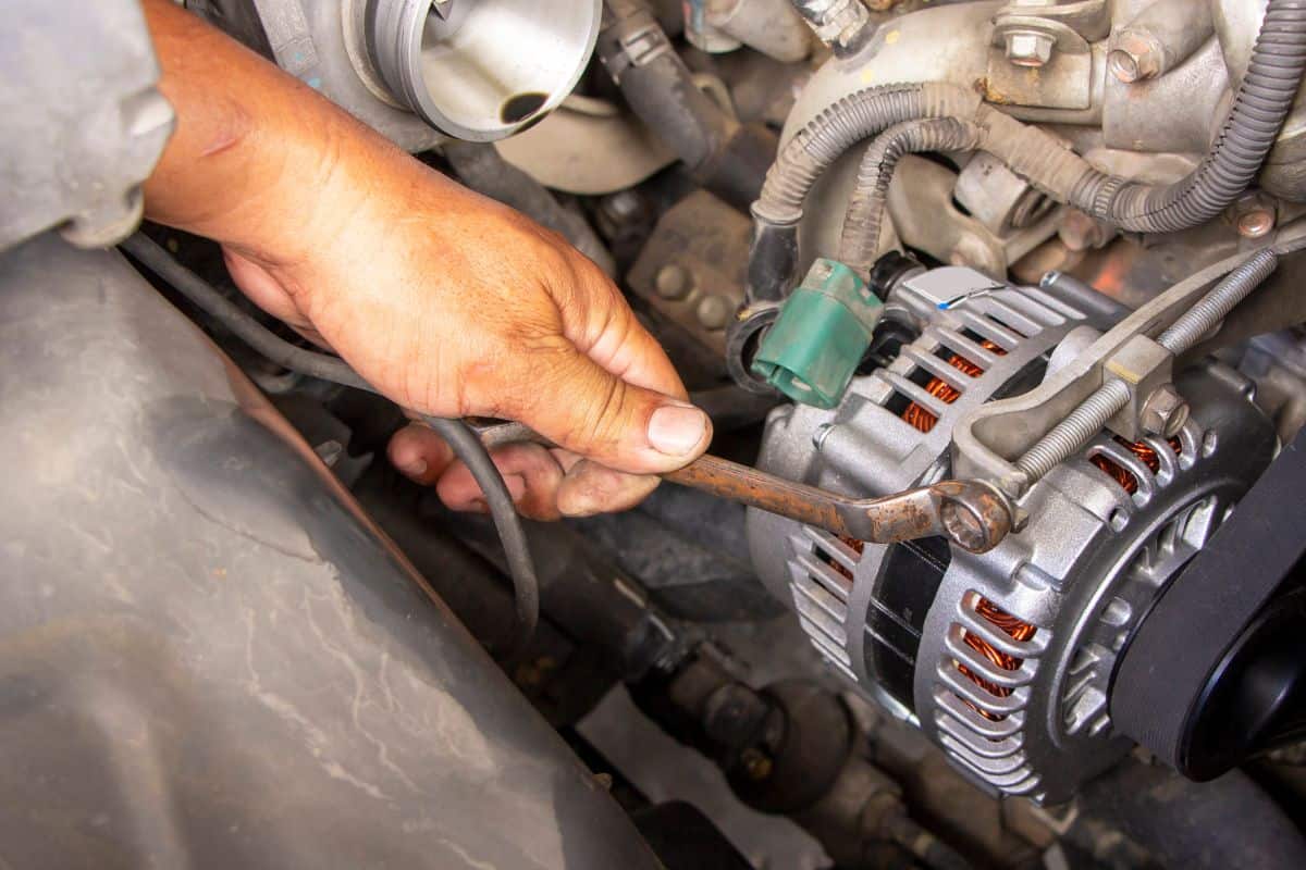 achanic or worker hand-holding wrench repair car alternator in a garage.