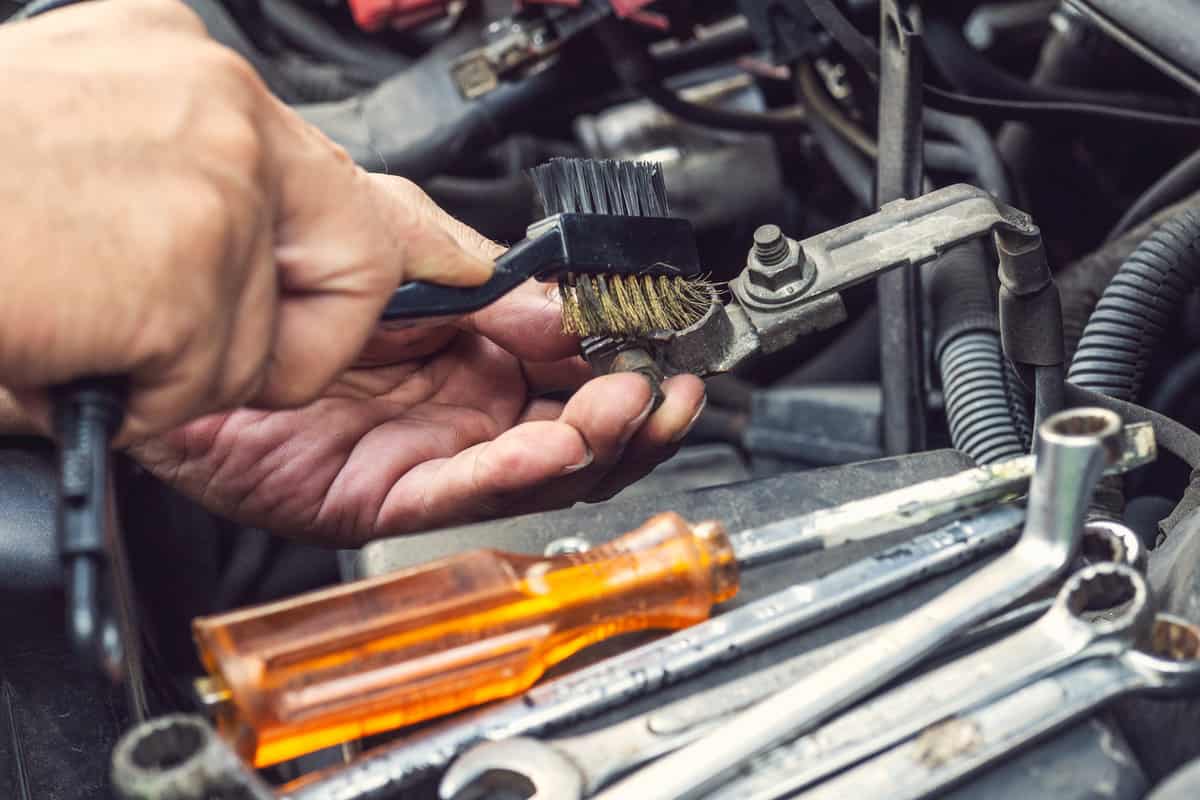mechanic cleaning a battery connections ,brush and insert the brush into the car's battery terminals,especially if terminals are corroded, will help ensure the battery lasts longer and performs well