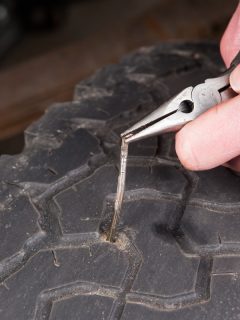 Mechanic's hands, are using needle nose pliers, to remove a nail which has punctured a vehicle tire., How Long Can You Drive With A Nail In Your Tire?