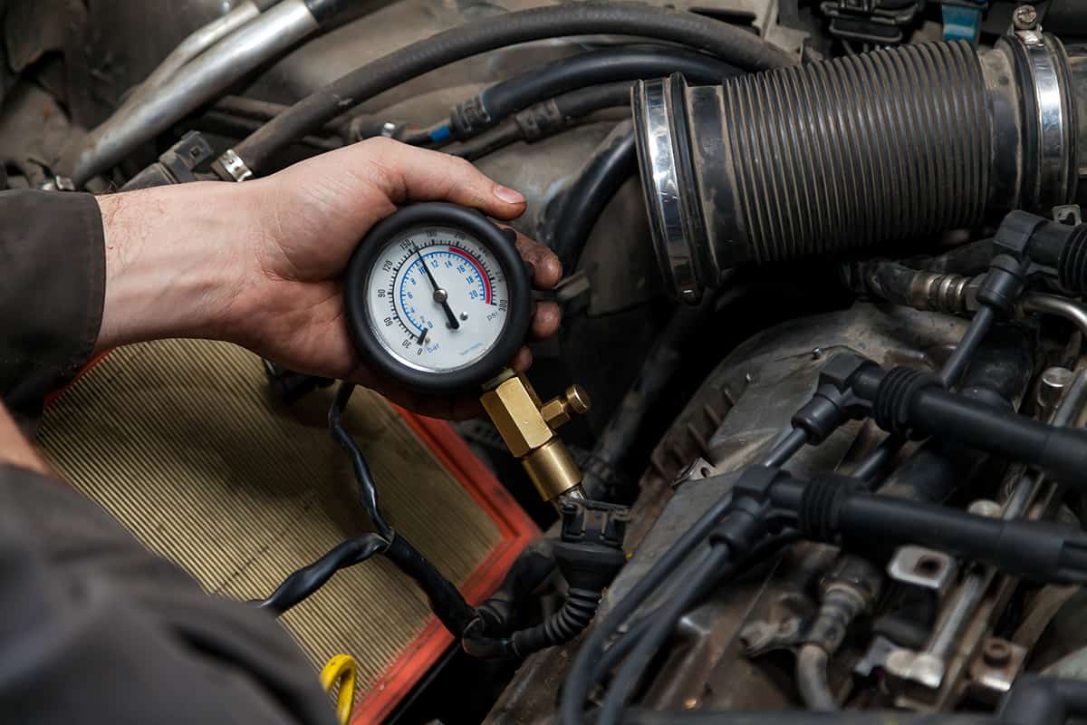 A male mechanic measures the compression in the cylinder of a car engine using a barometer with a scale and an arrow during diagnosis and repair in a workshop for vehicles