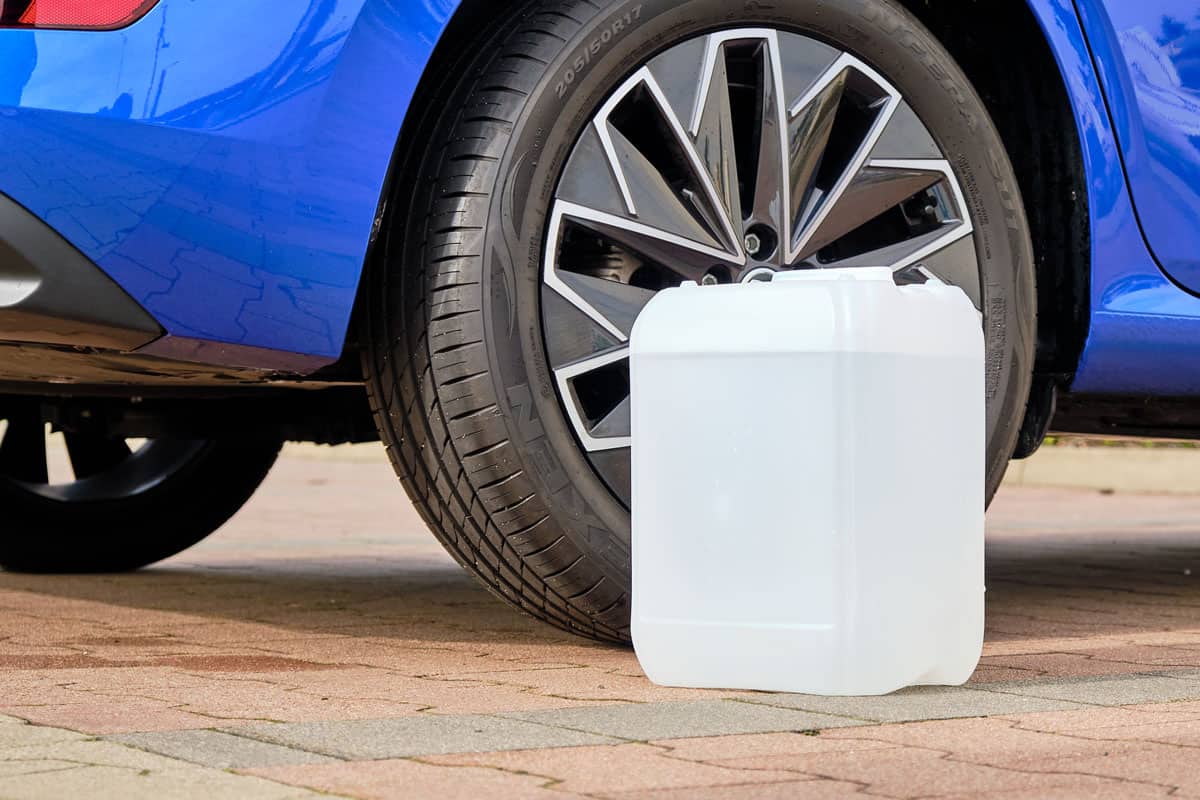 A white canister with a diesel exhaust fluid DEF for reduction of air pollution standing near a blue car