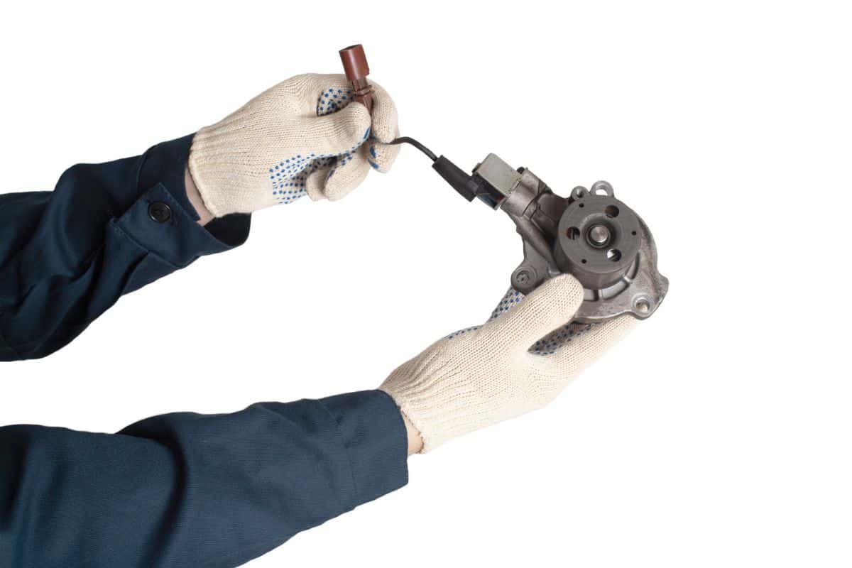 An auto mechanic holds a faulty car cooling system pump that drives coolant, white background, isolate. Regulations for replacing the auto pump, background