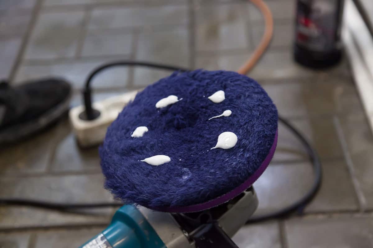 Blue round brush of industrial polishing machine with white cream before applying polishing compound to car close-up in workshop