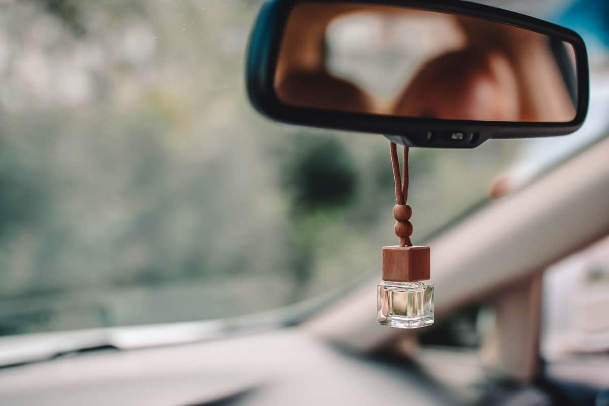 Little glass bottle with wooden lid and yellow aromatic liquid automobile freshener on car mirror
