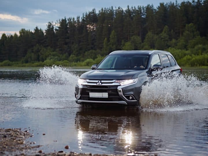 Mitsubishi Outlander car rides on the river, flying spray of water in the headlights of the car, against the backdrop of the summer landscape in the evening, Mitsubishi Outlander Beeping While Driving - Why And What To Do