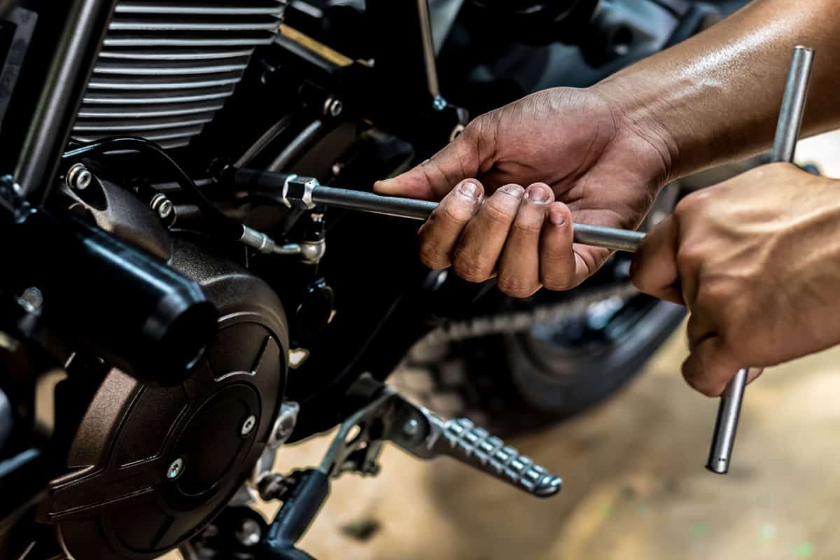 People holding hand are repairing a motorcycle.