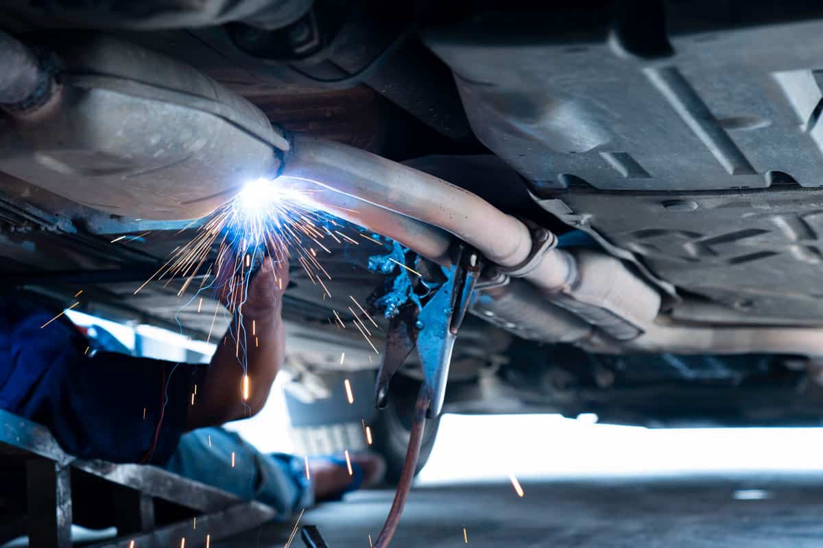 The hand of a mechanic or welder is fixing a car exhaust system by welding the exhaust pipe
