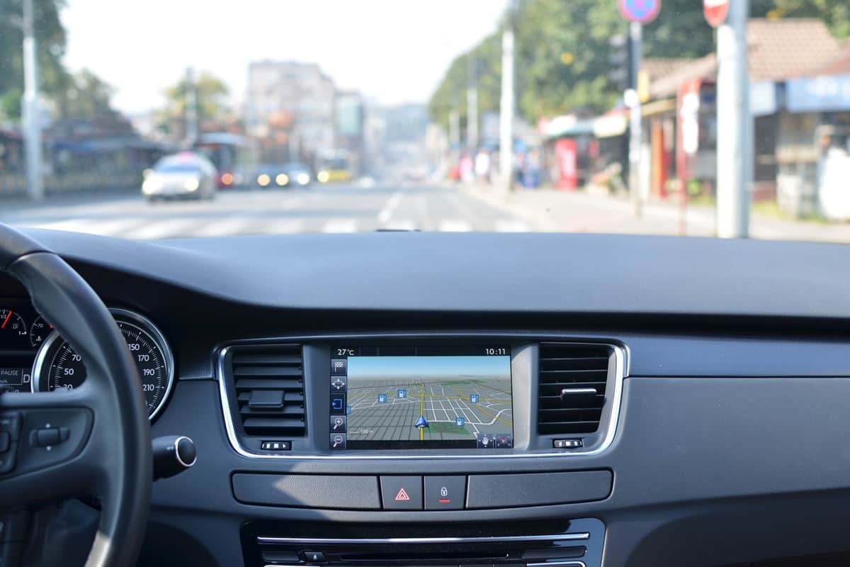 View from inside a car on a part of dashboard with a navigation unit and blurred street in front of a car