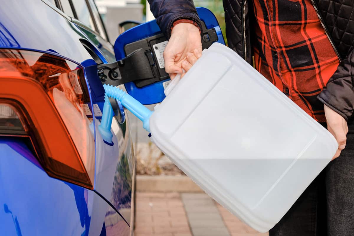 Woman filling a diesel engine fluid from canister into the tank of blue car