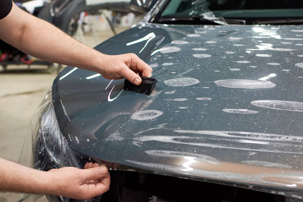 man installing cling film on the hood of the glossy grey car paint