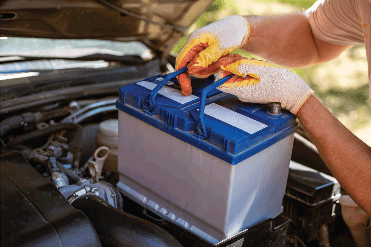 A man removes a battery from under the hood of a car