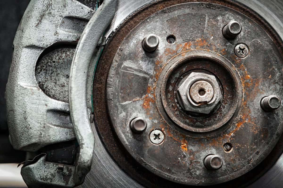 Close-up of the replacement of the old front brake disc, brake caliper and hub nut on a car lifted on a lift with the help of a pneumatic wrench in a car repair shop. Auto mechanic repair.
