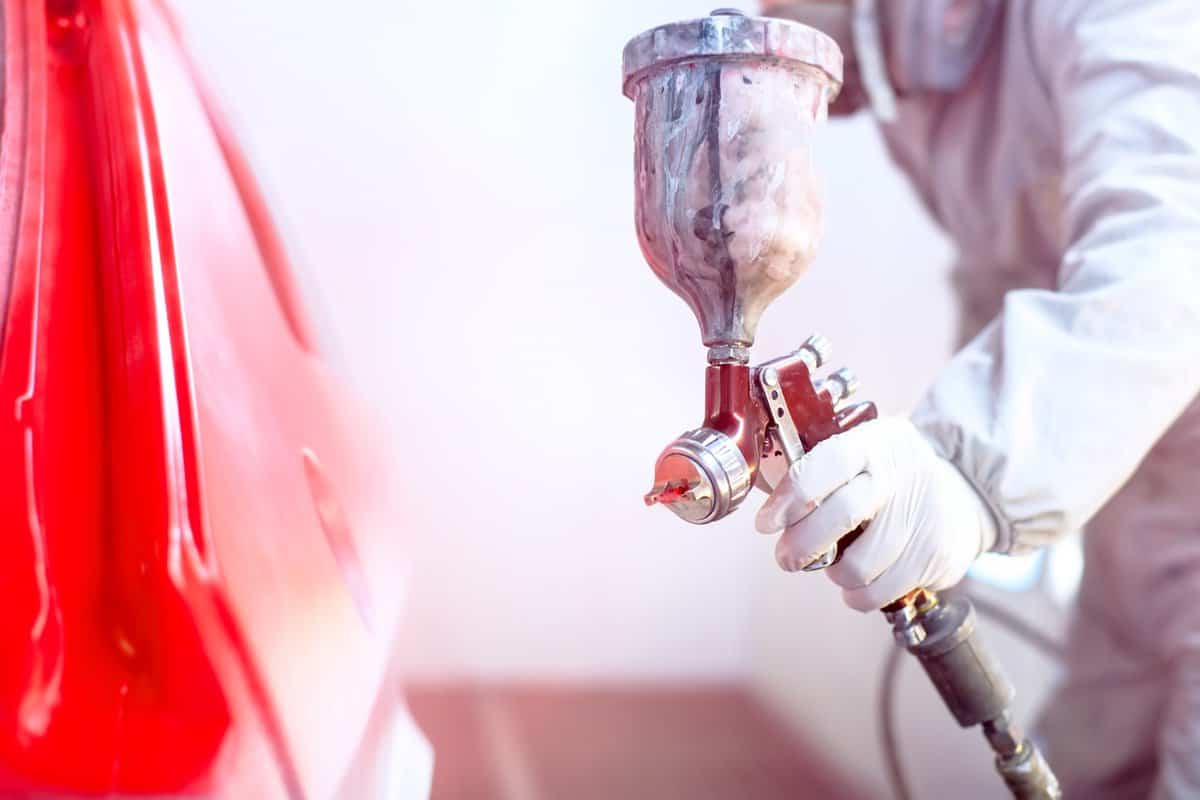Close-up of spray gun with red paint painting a car in special booth 
