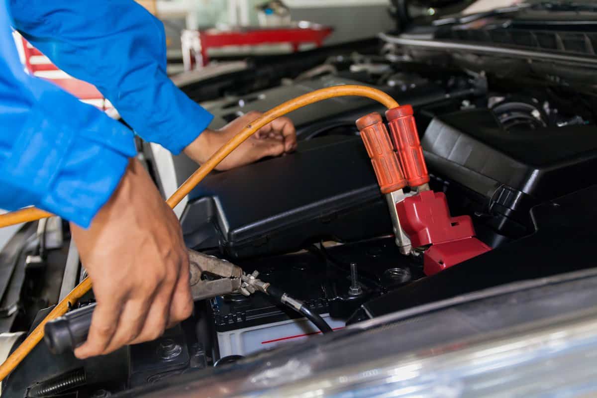 Mechanic attaching jumper cables with battery car - closeup